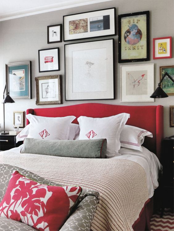 a grey bedroom spruced up with lots of artworks and a red upholstered bed
