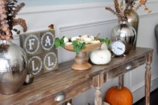 17 a fall console with orange and white pumpkins, fall leaves and dried blooms and firewood in a metal bathtub