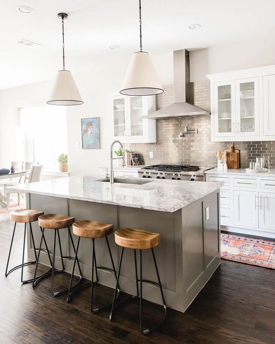 a white kitchen with a grey kitchen island, a stone countertop and a metallic tile backsplash add interest