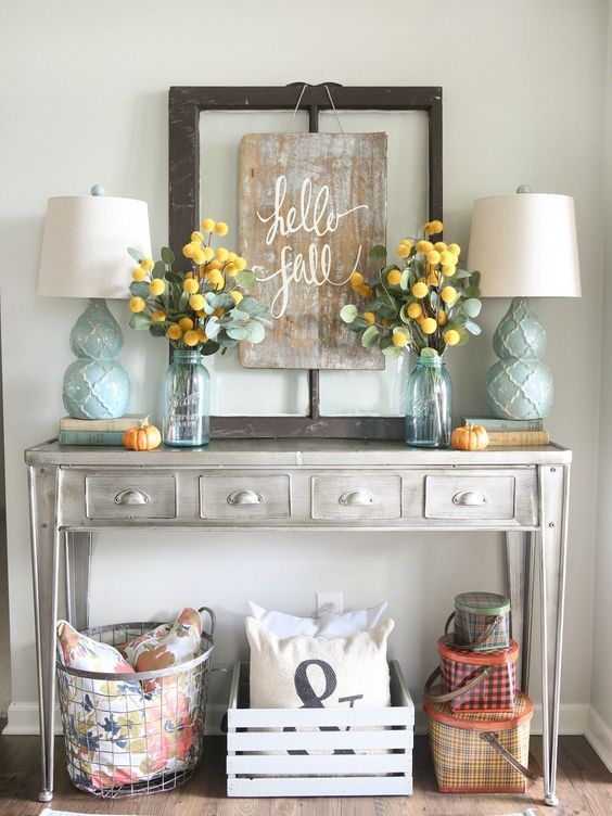 a grey console table with aqua lamps, a worn wooden sign and eucalyptus and craspedia arrangements