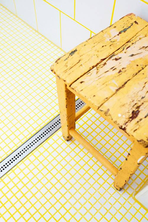 Little white tiles and large ones are tied with each other usign bright yellow grout plus a yellow stool that echoes with it