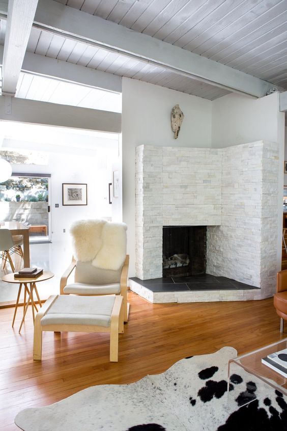 a cozy fireplace nook with a leather chair and a footrest plus a cowhide rug for reading