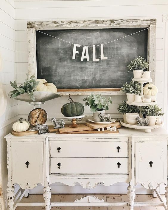 a vintage carved console table with white and grene pumpkins, greenery in pots and vintage figurines