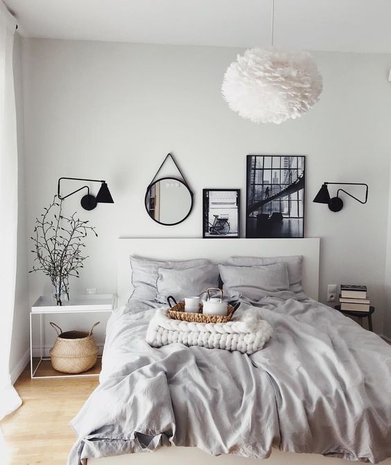 a light grey bedroom enlivened with some artworks, a mirror and sconces in black for depth