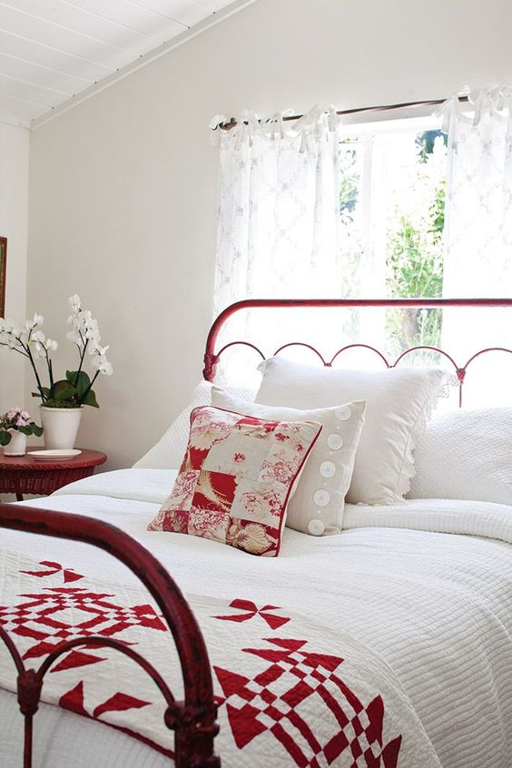 a white bedroom with a red metal frame bed and a matching wicker nightstand