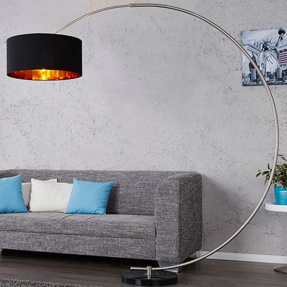 a statement floor lamp with a base on the floor and a rounded long 'leg' and a large black and metallic lampshade