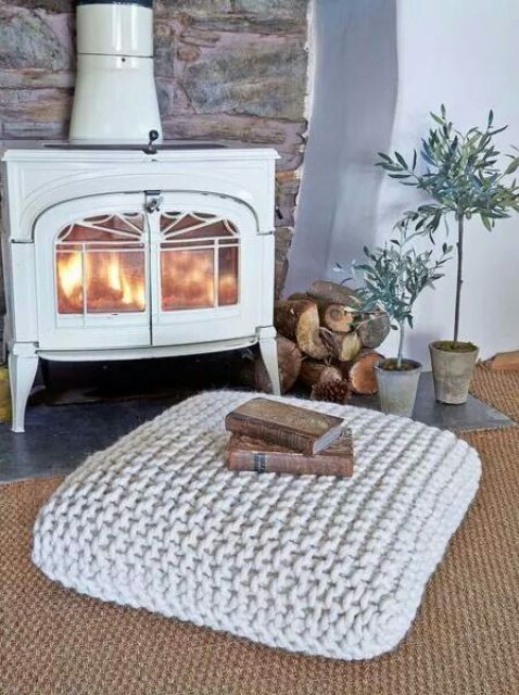 a traditional space by a large hearth with a rug and a chunky knit cushion on the floor