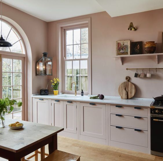 a beautiful dusty pink kitchen with matching cabinetry, shaker cabinets, black handles, white stone countertops and a shelf