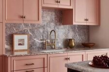a chic pink kitchen with a grey stone backsplash and countertops, brass and gold touches and black is pure elegance