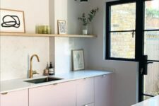 a contemporary kitchen with pale pink lower cabinets, white stone countertops and a backsplash, a long shelf and potted greenery