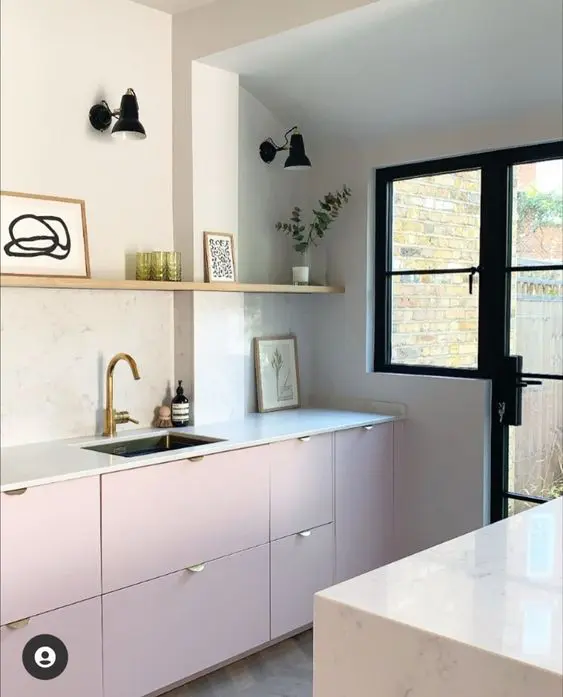 A contemporary kitchen with pale pink lower cabinets, white stone countertops and a backsplash, a long shelf and potted greenery