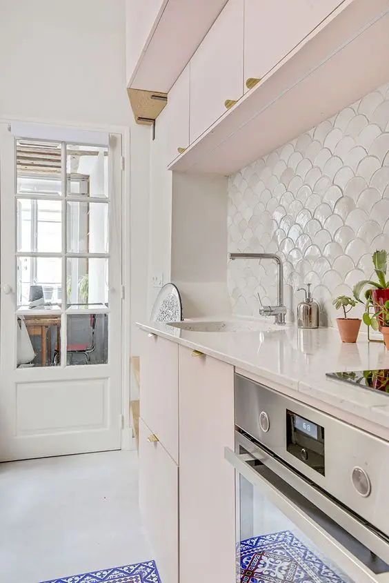 a delicate blush kitchen with a white scallop tile backsplash, white stone countertops, potted greenery