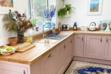 a dusty pink lower cabinet kitchen with butcherblock countertops, some decor and greenery and a skylight