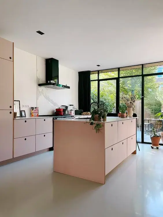 A light filled pink kitchen with MDF cabinets, neutral countertops, a white marble backsplash and black appliances