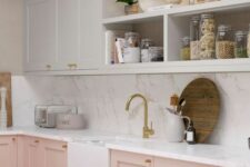 a lovely and welcoming kitchen with pink and white cabinets, open storage compartments and a white stone backsplash and countertops