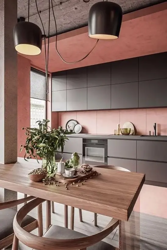 A minimalist kitchen in pink, with sleek graphite grey cabinetry, a concrete ceiling and a small dining space