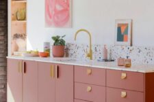 a modern and stylish pink kitchen with a terrazzo backsplash and countertops, gold hardware and a faucet, a niche for storage