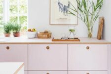 a pale pink kitchen with MDF cabinets, white stone countertops, potted herbs and lots of natural light