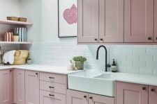 a pale pink kitchen with shaker style cabinets, a white subway tile backsplash and white countertops, open shelves and a skylight