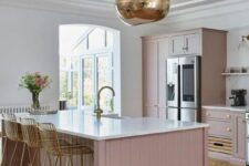 a pale pink kitchen with shiplap cabinets and white stone countertops plus a white stone backsplash, a gold pendant lamp and matching tall stools