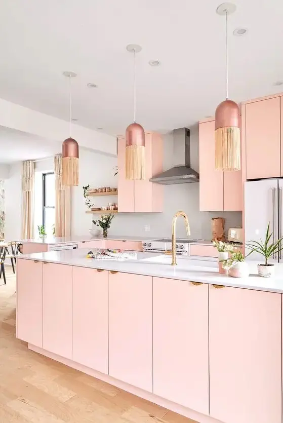 a pastel pink kitchen with plain cabinets, a large kitchen island, a white backsplash and coutnertops, pendant lamps with fringe