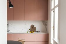 a refined minimalist pink kitchen with a sleek white marble backsplash and countertops, a black table and woven chairs