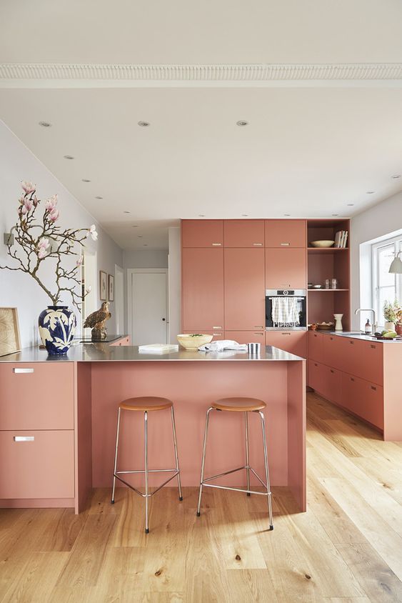 A salmon pink kitchen with sleek cabinets, a large kitchen island, stools and beautiful and elegant decor