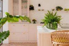 a welcoming pink kitchen with shaker cabinets, a large kitchen island, white stone countertops, a ledge with potted greenery and rattan stools