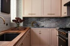 an eclectic kitchen with blush cabinets, a white tile wall, a grey marble backsplash and dark appliances