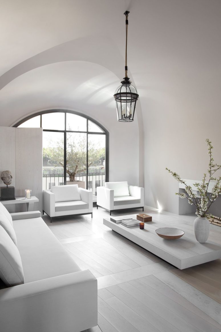 The living room is a light-filled space with white furniture and much light coming through an arched window