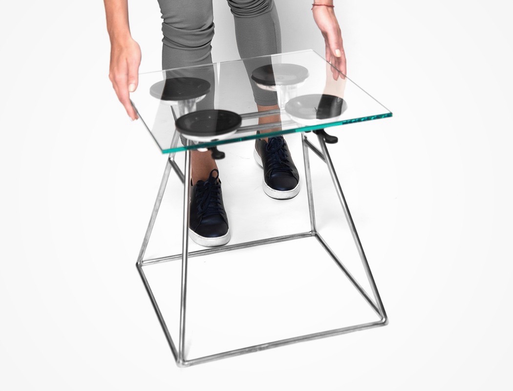 The stool features a metal base, some suction cups and a glass top or seat