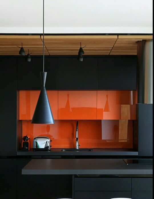 a minimalist kitchen in black and orange, with a glass backsplash and cool pendant lamps in black