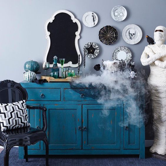 a vintage turquoise console table with a white and turquoise pumpkin, an assortment of black and white decorative plates and smoke comign from a cauldron