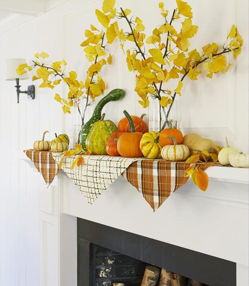 a fall mantel with a lot of pumpkins and gourds and yellow leaves in clear vases
