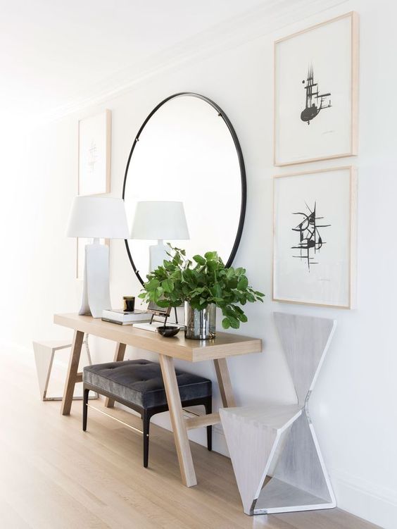 a large round mirror in a black frame and a dark upholstered bench stand out in a neutral space