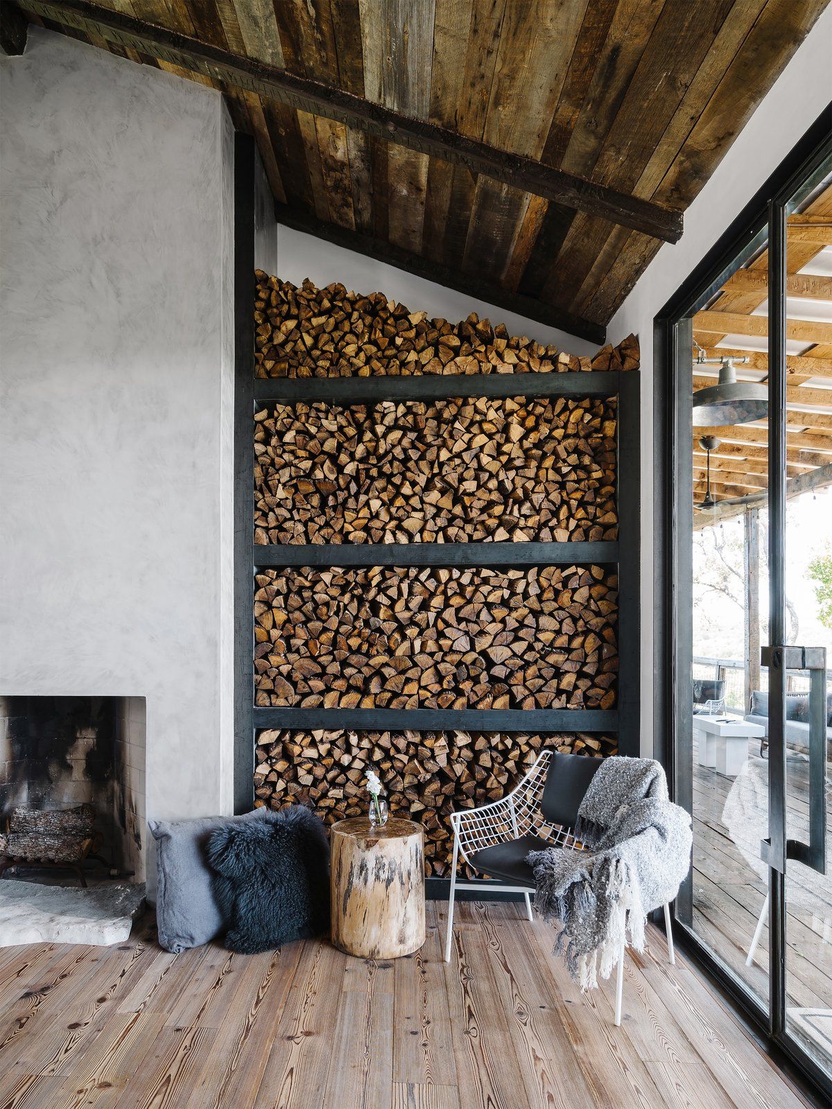 The living room features a concrete clad fireplace, a sitting zone by the window and a firewood storage