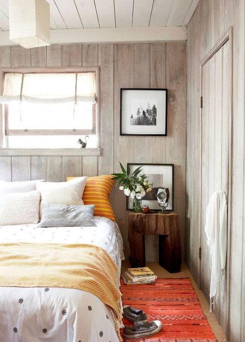 a cozy bedroom with whitewashed wood walls and ceiling spruced up with colorful textiles
