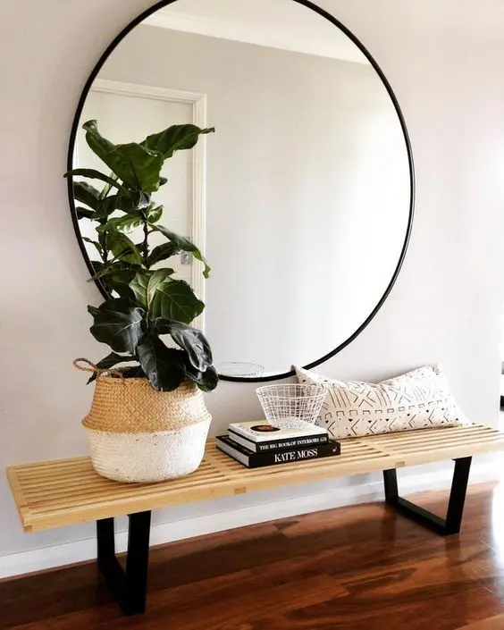 a large round mirror in a black frame and a wooden bench for a simple boho chic space
