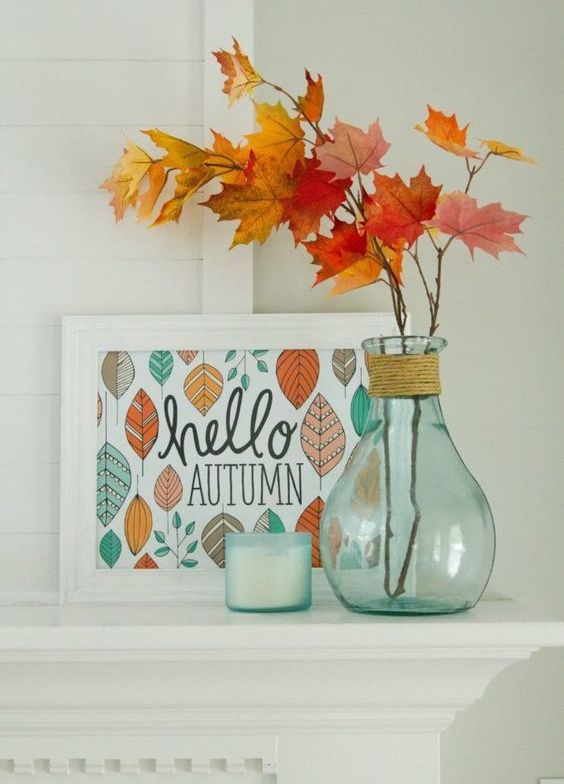 a stylish display with a sign, some fall leaves in a clear vase and a candle in opaque glass