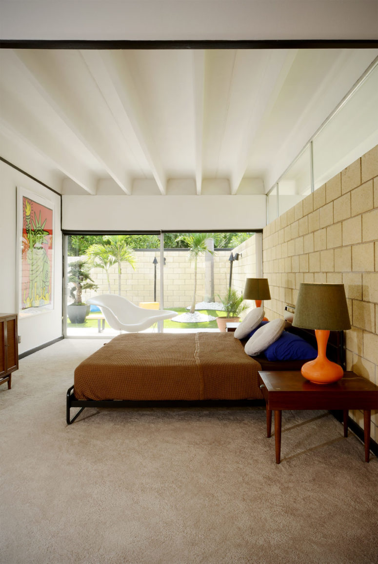 The master bedroom is opened up to outdoors with glass doors, there's colorful furniture and an artwork