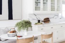 06 a chic white kitchen with a comfy dining nook, a banquette seating, wooden chairs and an oval table