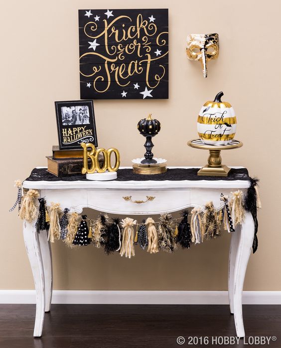 a spooktacular console with fake pumpkins, a tassel garland, a sign and gold letters