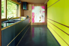 08 The kitchen is done in black with a contrasting neon yellow wall and a bold artwork