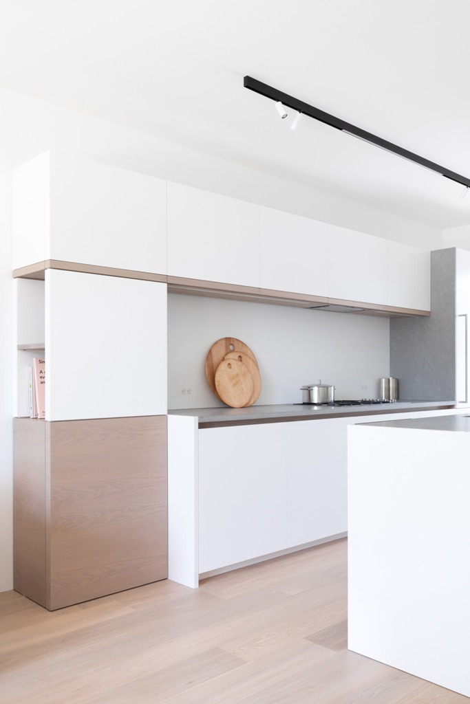 The kitchen is minimalist, in white and beige, with sleek cabinets and a concrete backsplash and countertops