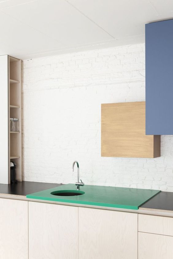 a plywood and a muted blue sleek cabinet on the wall and an emerald sink countertop for a color block effect