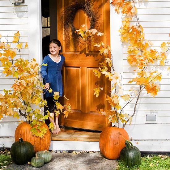 fall pumpkins with tall fall branches with leaves that imitate real trees on the porch