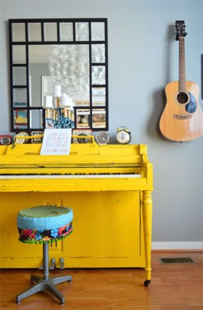 a bright yellow piano and a colorful stool, a framed mirror and a display of vintage clocks on the piano
