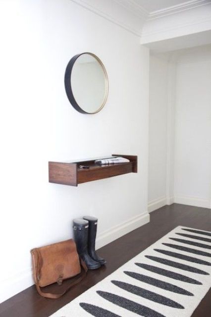 A tiny floating dark stained wood console and a mirror in a metallic frame for a chic look