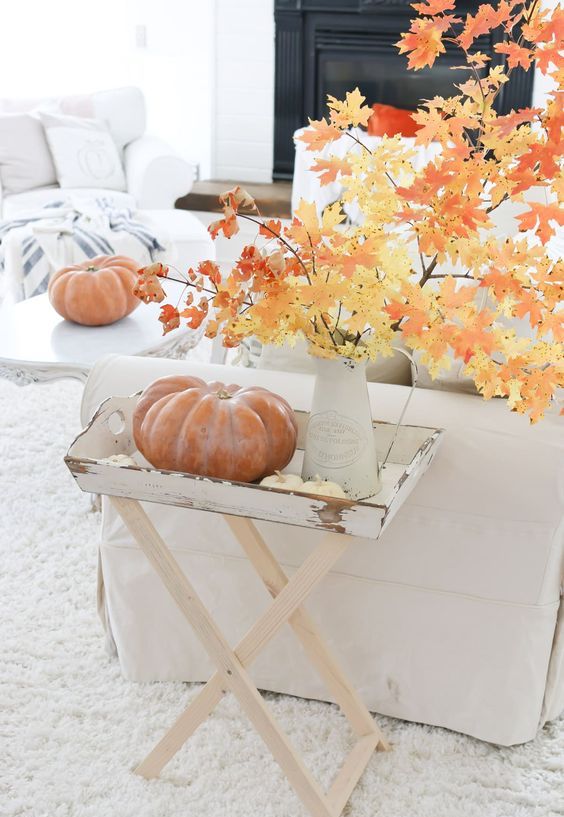 a vintage fall display with a little table filled with pumpkins and fall branches with leaves in a vase