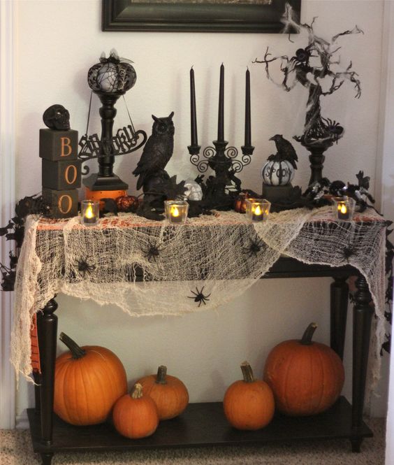 a Halloween console with spiderweb, fresh pumpkins, black candles and various figurines for a spooky feel